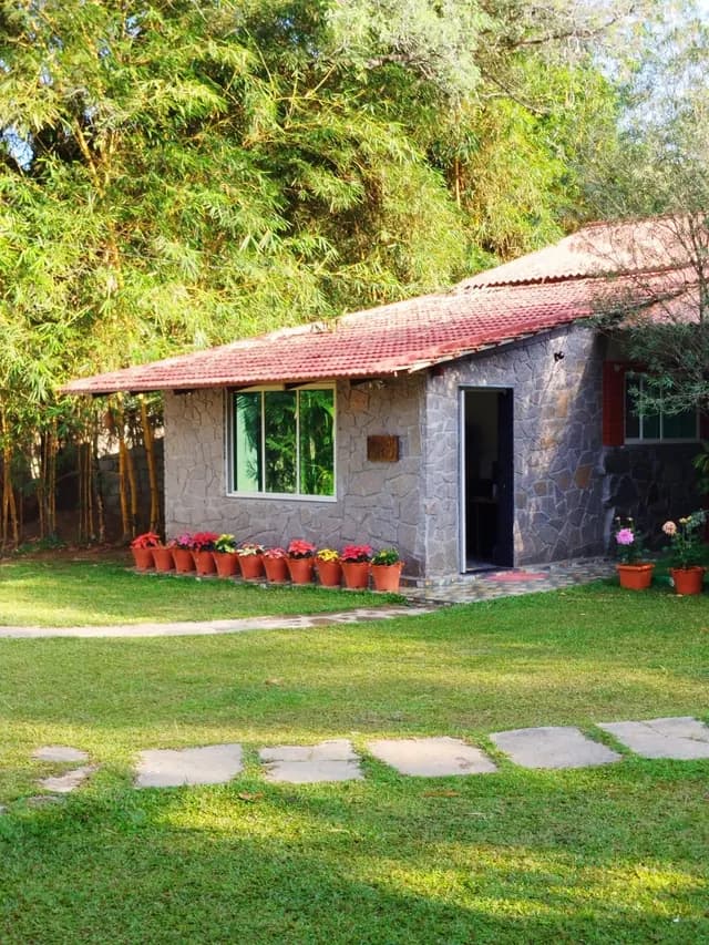 A tiled-roof cottage behind a lawn edged with potted flowers