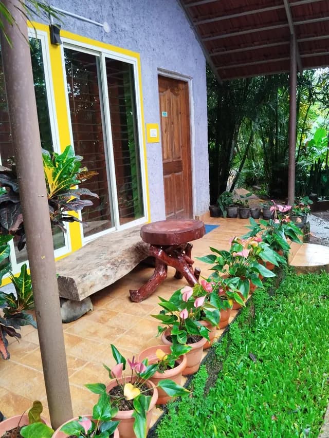 Cottage entrance with a yellow-framed window, a teak door and a low carved stool