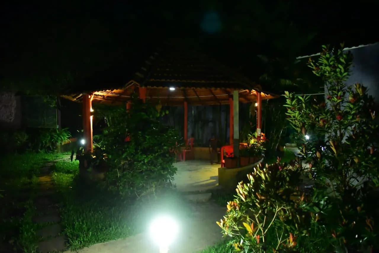 The gazebo lit from within at night, surrounded by planting